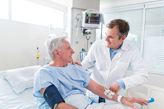 Male doctor talking to elderly male patient in hospital room