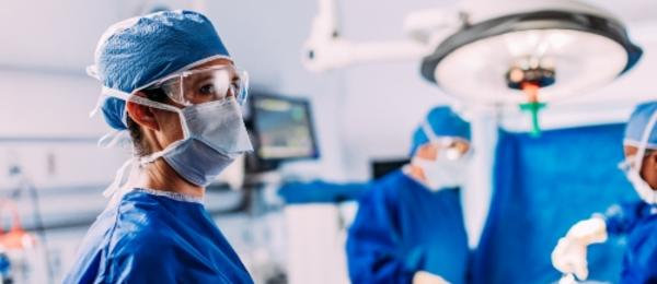 Female doctor in scurbs in a operating room with two doctors operating in the background